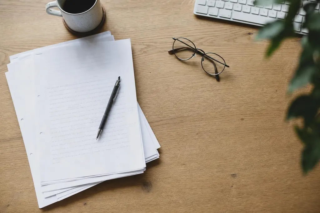 An overhead view of a desk with printed article drafts, reading glasses and a pencil